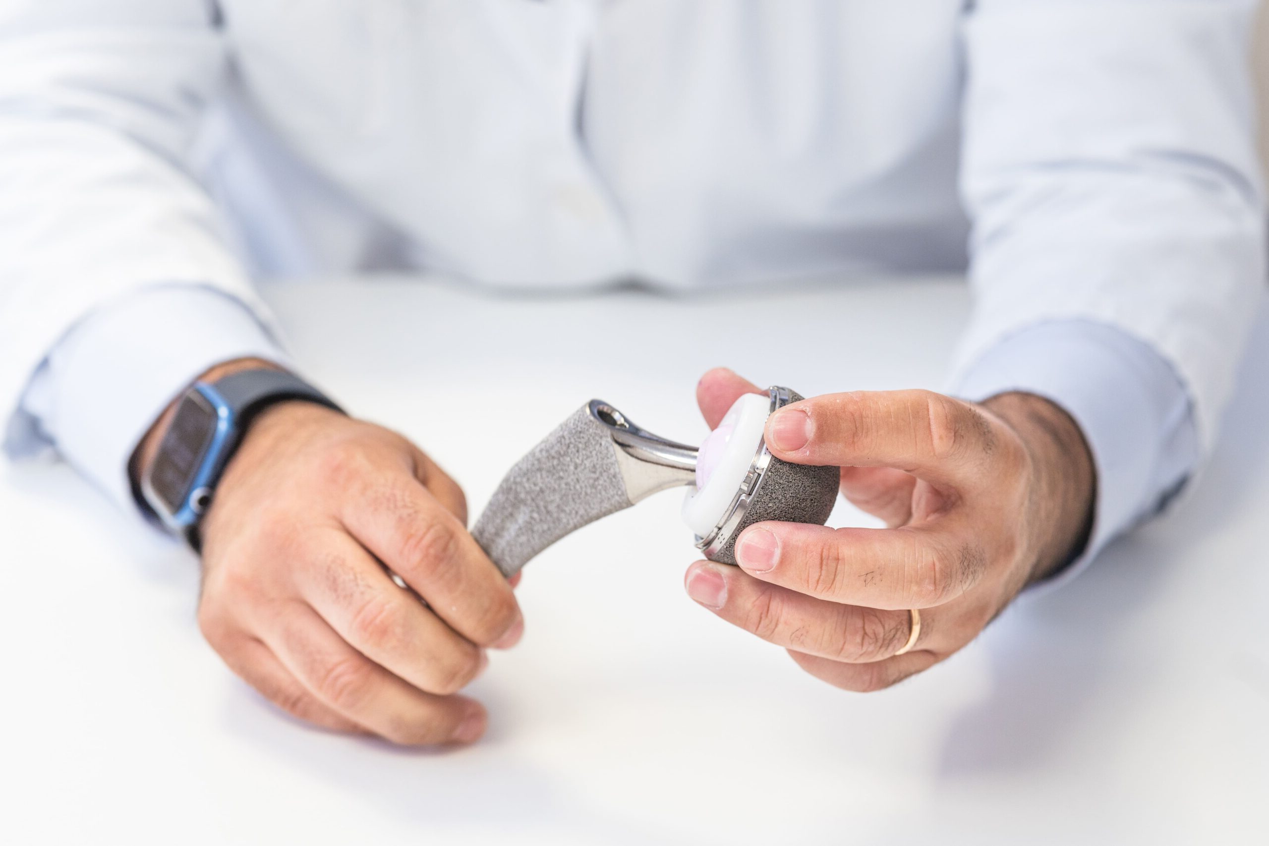 Close-up of a person holding a hip prosthesis, discussing potential complications.